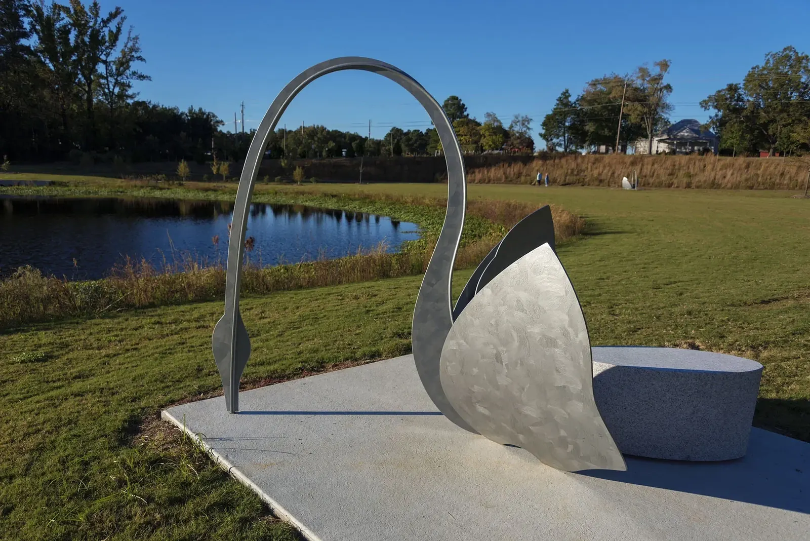 Painted steel swan with a long arched neck and broad wings around a granite bench beside the pond at Carpenter Park.