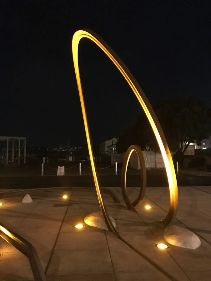 Tall illuminated steel loop with a smaller loop behind it, glowing gold against the night sky at Fort Mason.